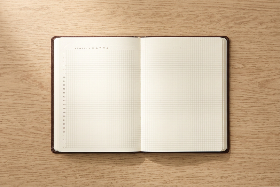 Brown Hibino A6 Free Diary open to its undated two-page spread on a pale oak desk.