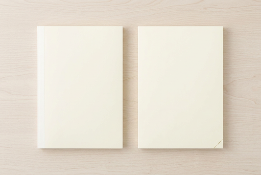 Overhead comparison of the ivory MD Notebook A5 and MD Notebook A5 Codex 1 Day 1 Page Dot Grid on a pale oak desk.