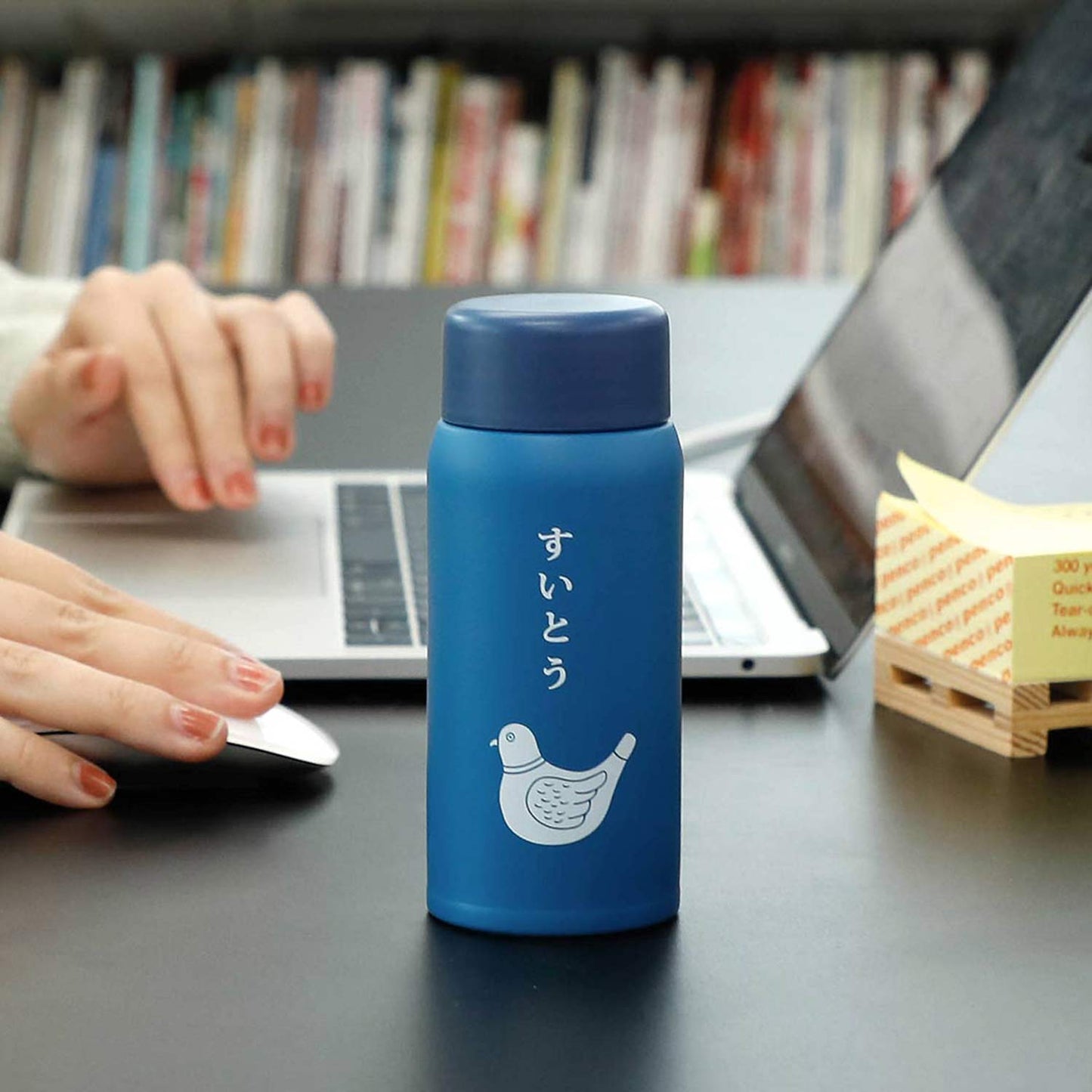 Blue thermos bottle on a desk with a person using a laptop in the background