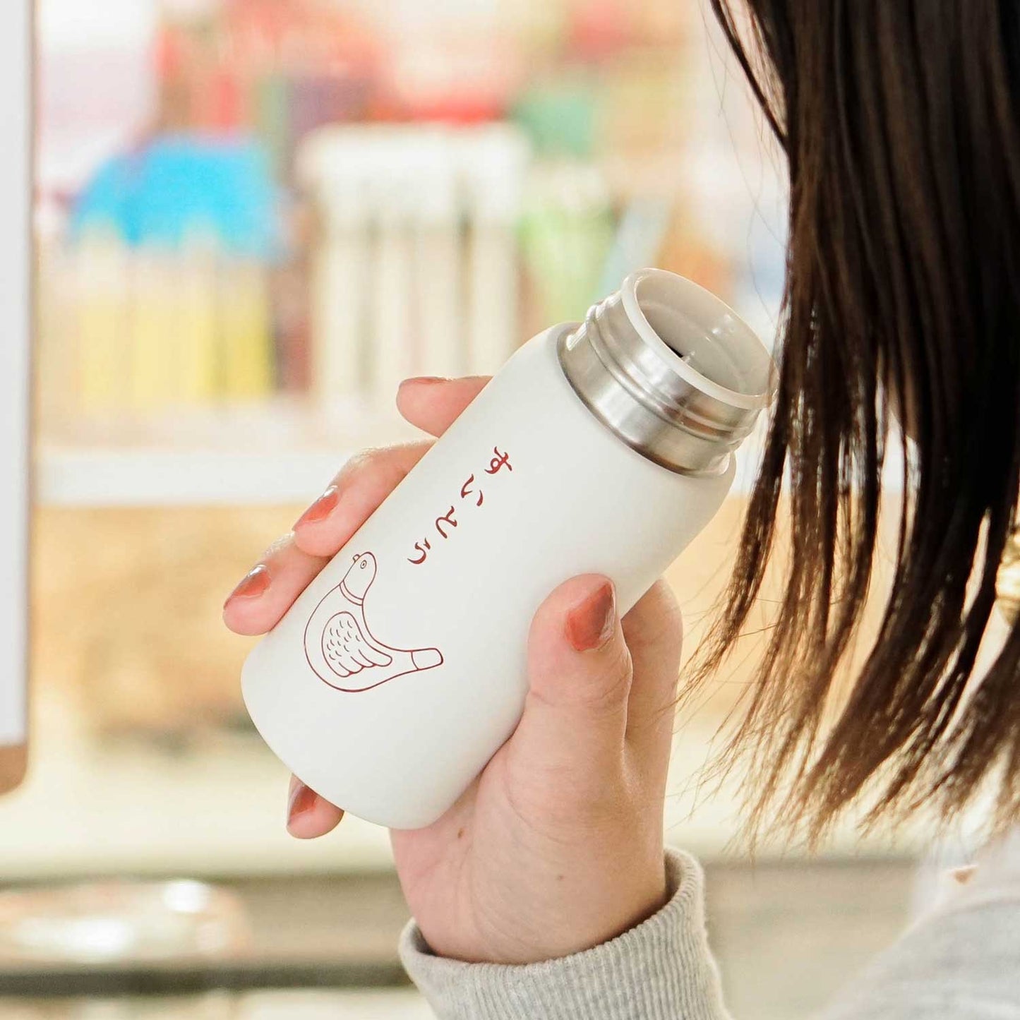 Person holding a white thermos with a design on a blurred background