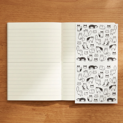 Use-case image: open lined MD A6 notebook and sticker sheet on a wooden desk