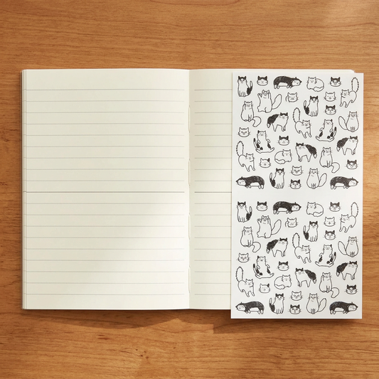 Use-case image: open lined MD A6 notebook and sticker sheet on a wooden desk